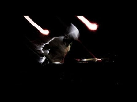 Andrew Hung performing, side on, black background wearing a hoody