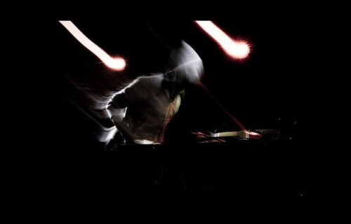 Andrew Hung performing, side on, black background wearing a hoody