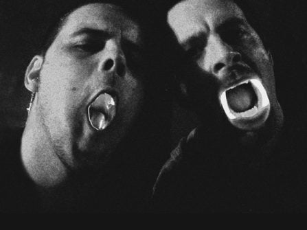 Ingen (left) and Savier (right) posing with heads tilted and lit up plastic teeth/mouths. black and white image.