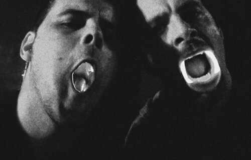 Ingen (left) and Savier (right) posing with heads tilted and lit up plastic teeth/mouths. black and white image.