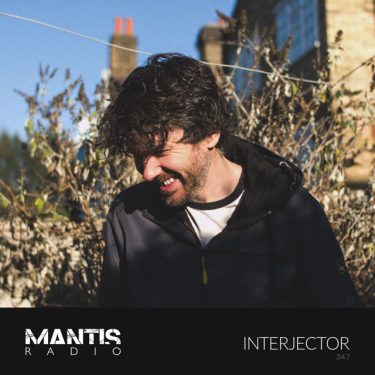 Interjector (Matt Faulkner) smiling with his head to the side in a garden with terrace housing behind him and a blue sky - Mantis Radio